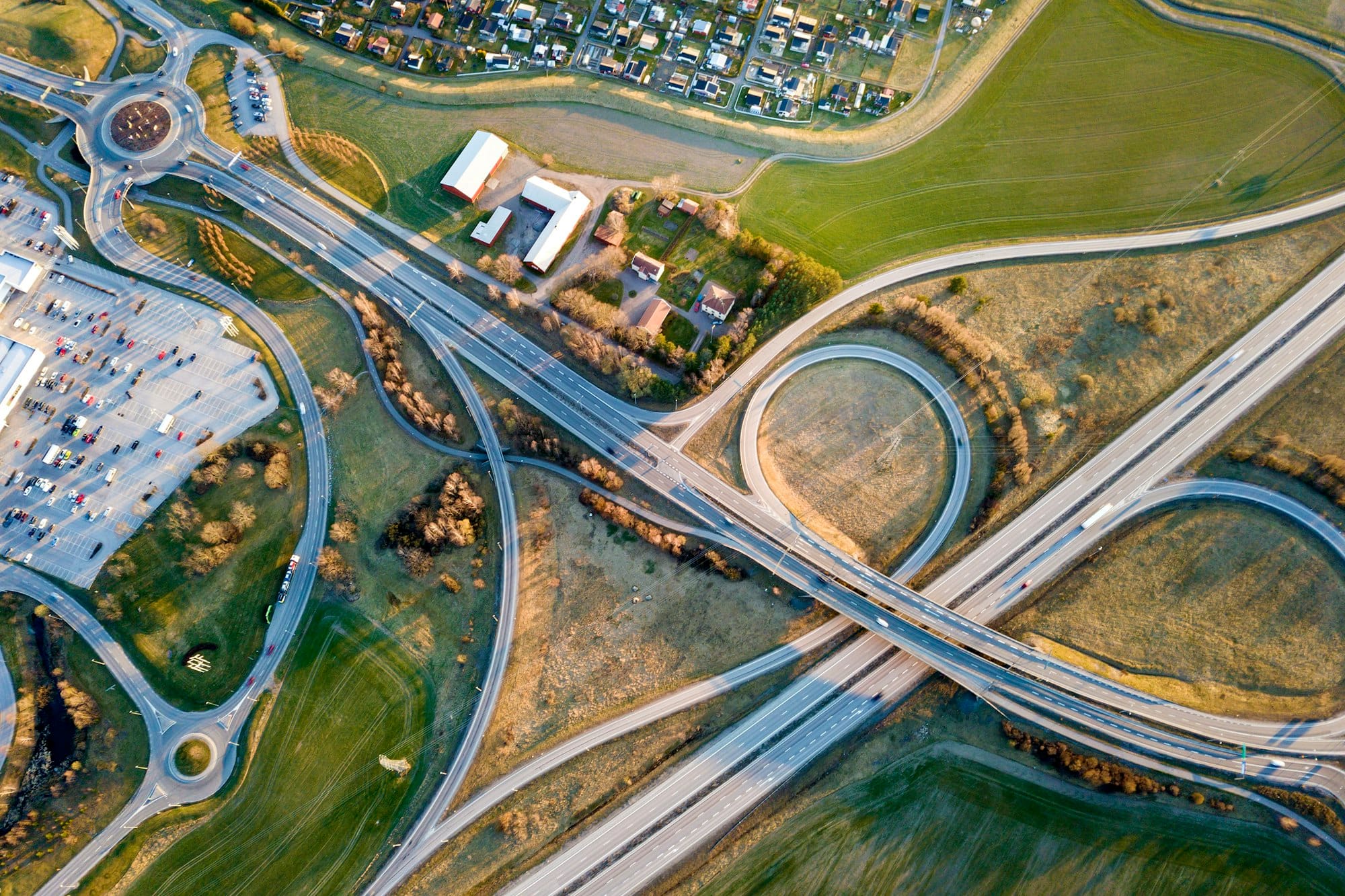 Aerial top view of modern highway road intersection, house roofs on spring green field