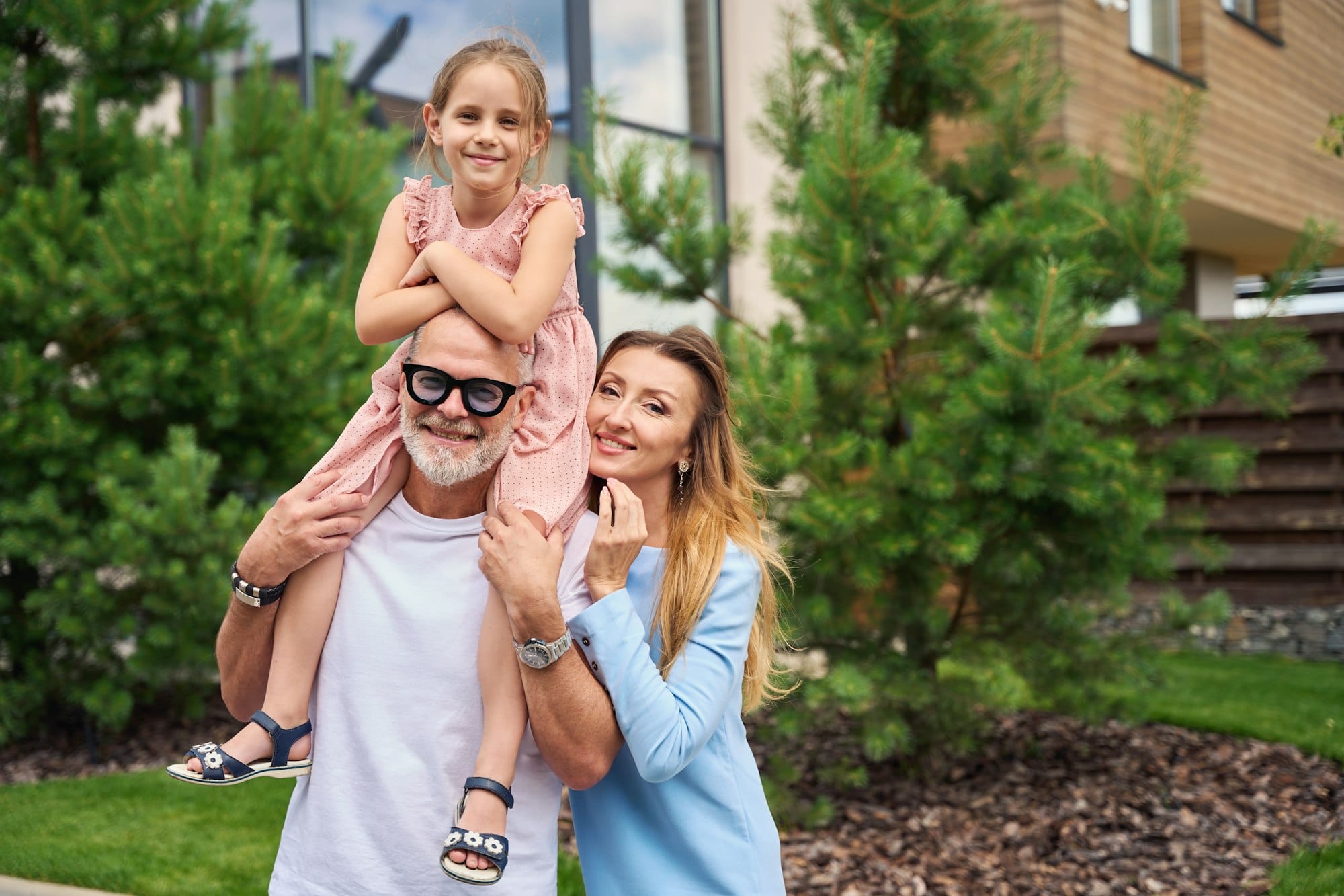 Happy young family stands in front of house with pines